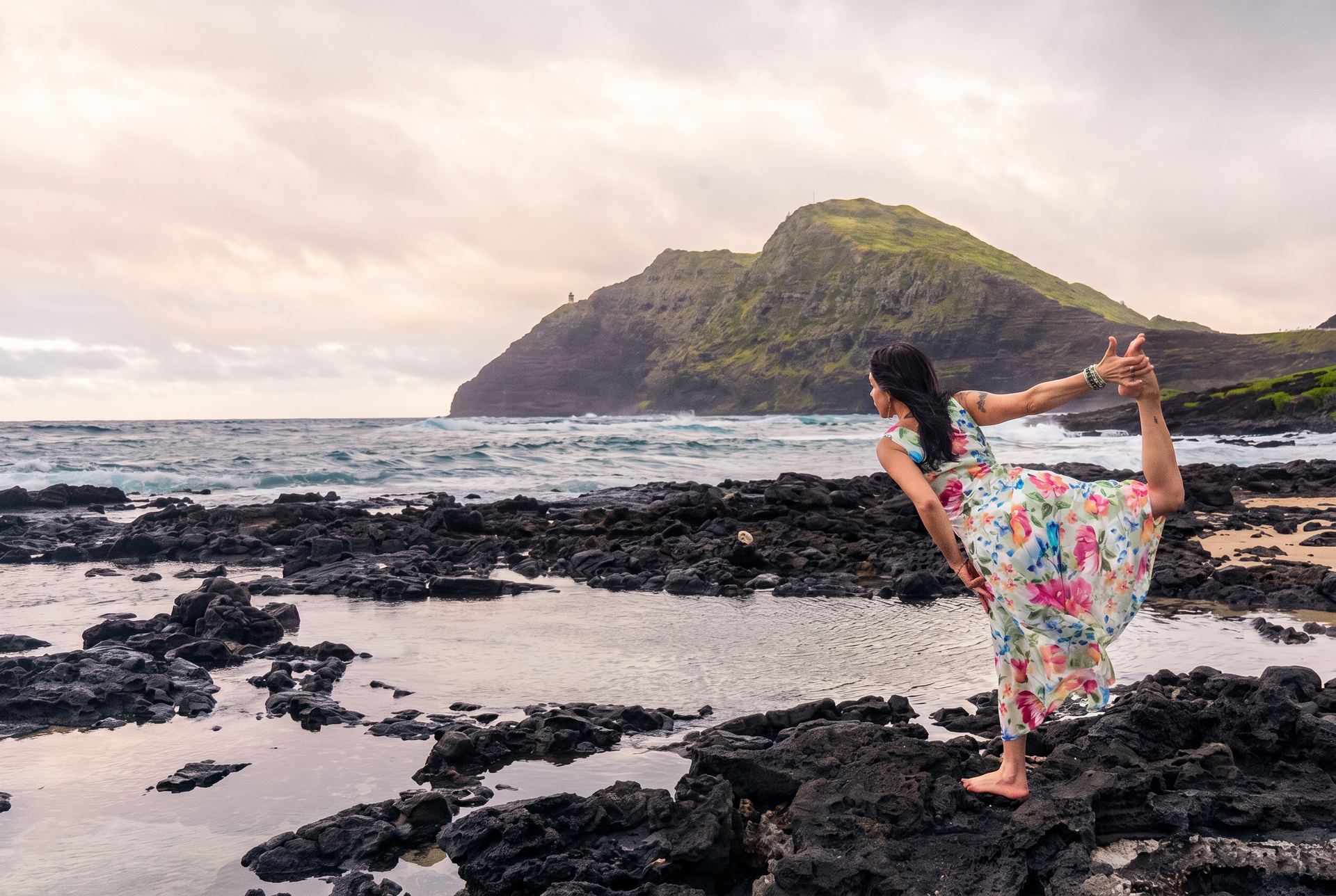 Marie in a standing yoga pose on the lava rock shoreline at golden hour in Hawaiʻi